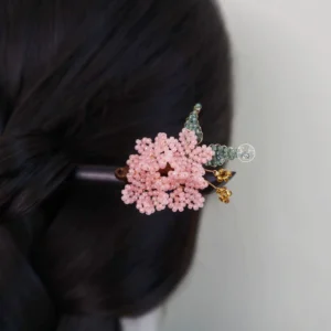 Cherry blossom Chinese hair stick worn in a twisted black hair updo, featuring pink beaded flower petals, green leaves, gold-tone pendants, and dark wooden pin