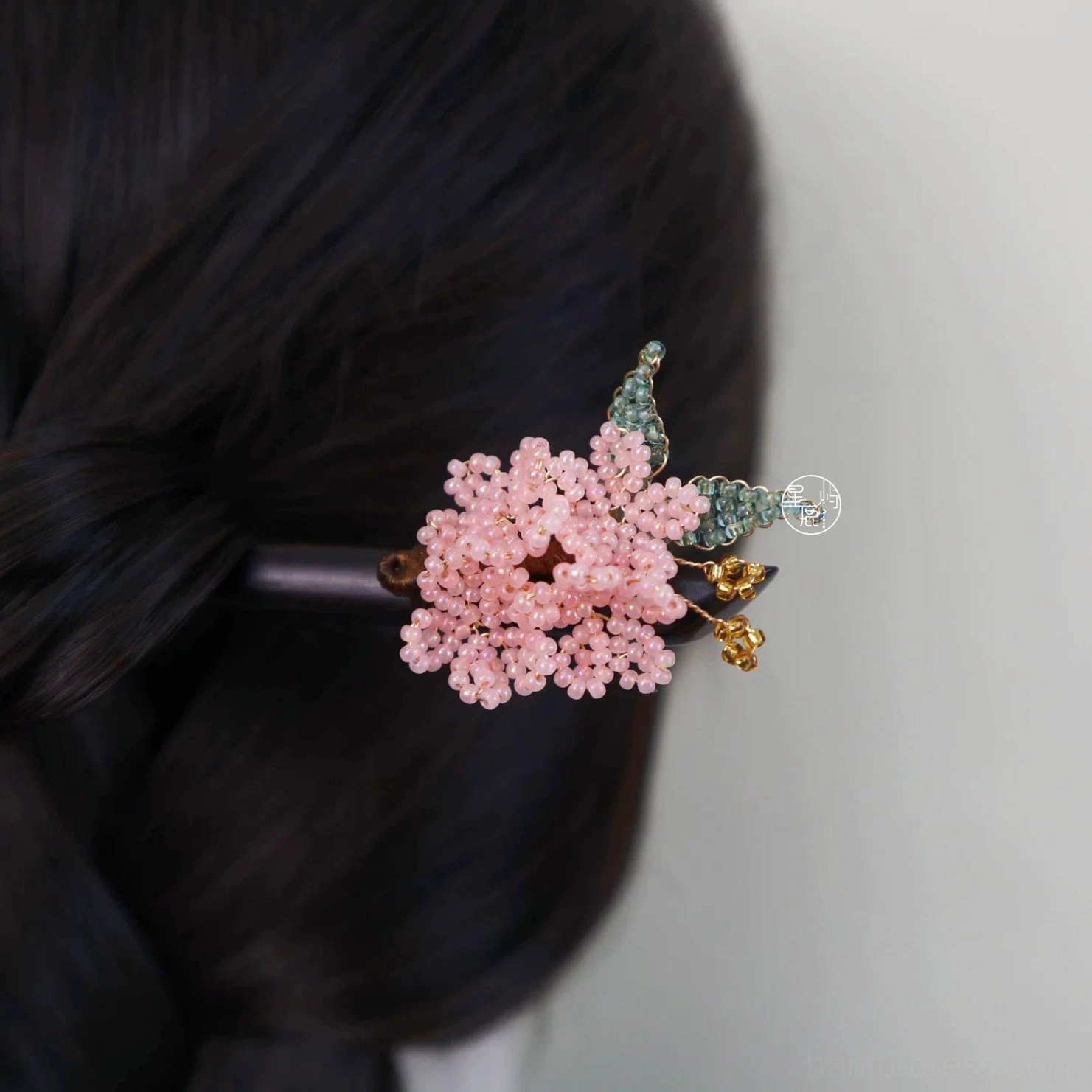 Cherry blossom Chinese hair stick worn in a twisted black hair updo, featuring pink beaded flower petals, green leaves, gold-tone pendants, and dark wooden pin