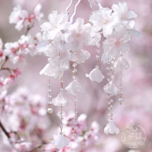 Cherry blossom Chinese hair stick with translucent pink resin flowers and delicate metal tassels against a soft blurred spring blossom background