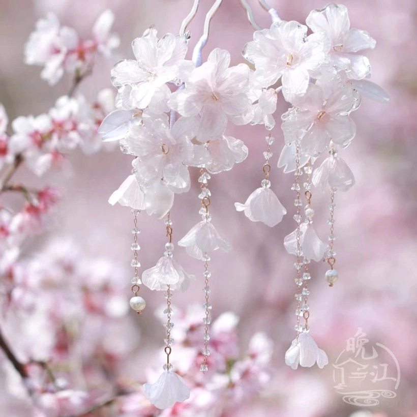 Cherry blossom Chinese hair stick with translucent pink resin flowers and delicate metal tassels against a soft blurred spring blossom background