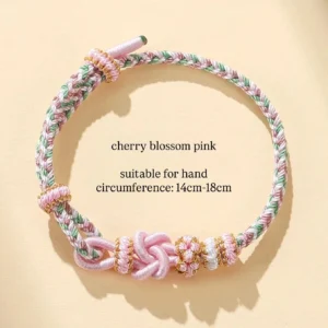 Cherry blossom pink handwoven Chinese knot bracelet with pink green and white braided cord floral woven charms and gold trim on a light beige background