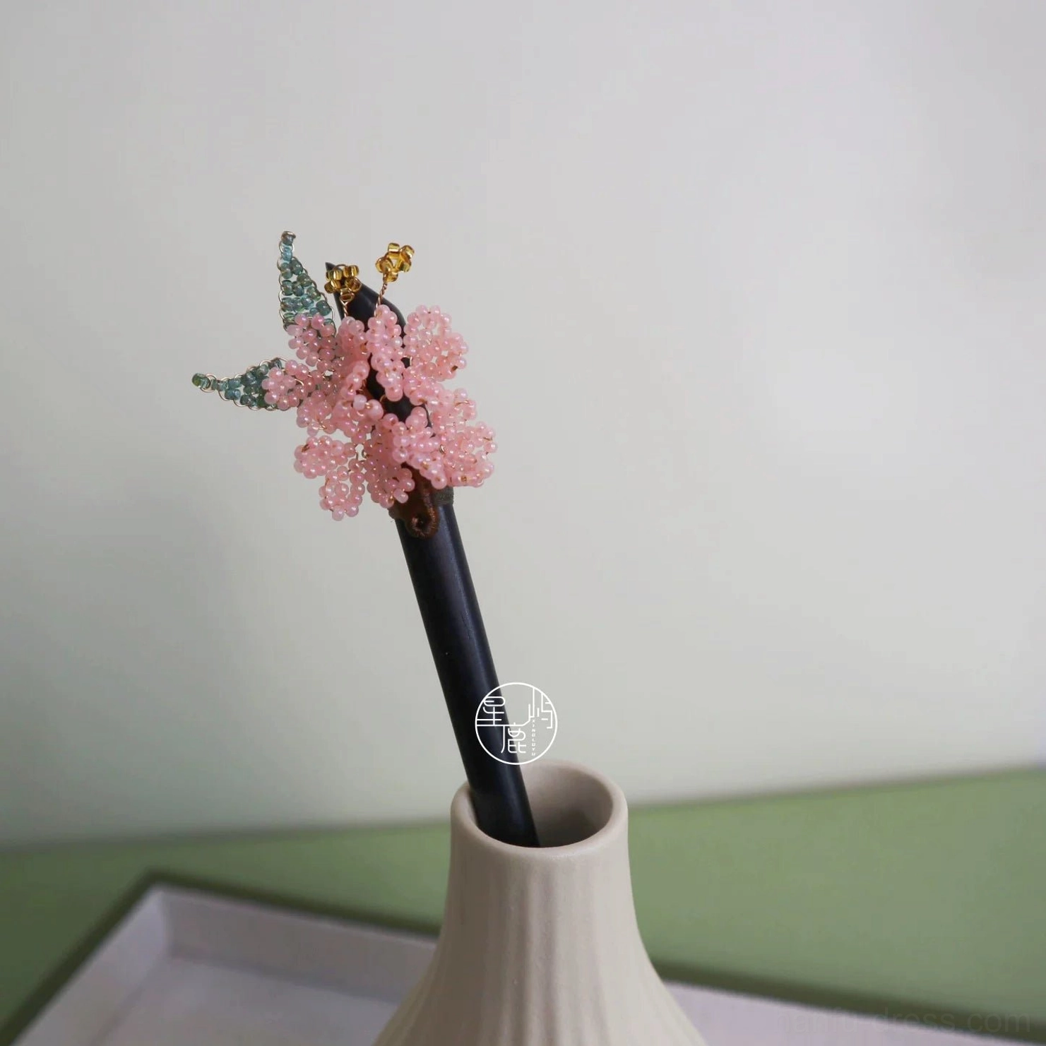 Cherry blossom Hanfu hair accessory displayed in a white ceramic vase, showing the dark wooden hair stick, pink floral beadwork, green leaves, and gold-tone dangles