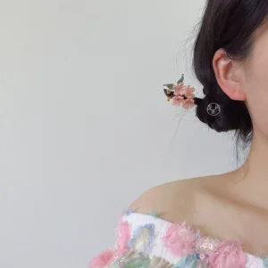 Side rear view of a woman wearing a cherry blossom Hanfu hair stick in a low side bun with pink flower beads, green leaf details, and dangling gold-tone ornaments