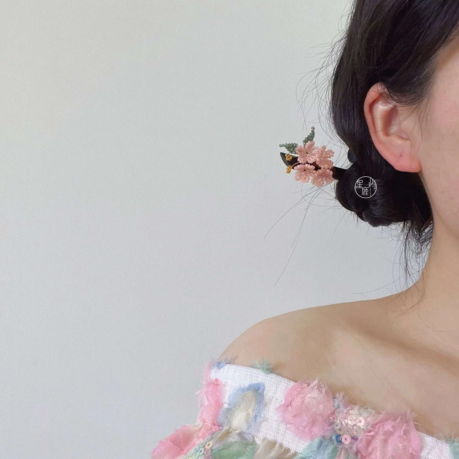 Side rear view of a woman wearing a cherry blossom Hanfu hair stick in a low side bun with pink flower beads, green leaf details, and dangling gold-tone ornaments
