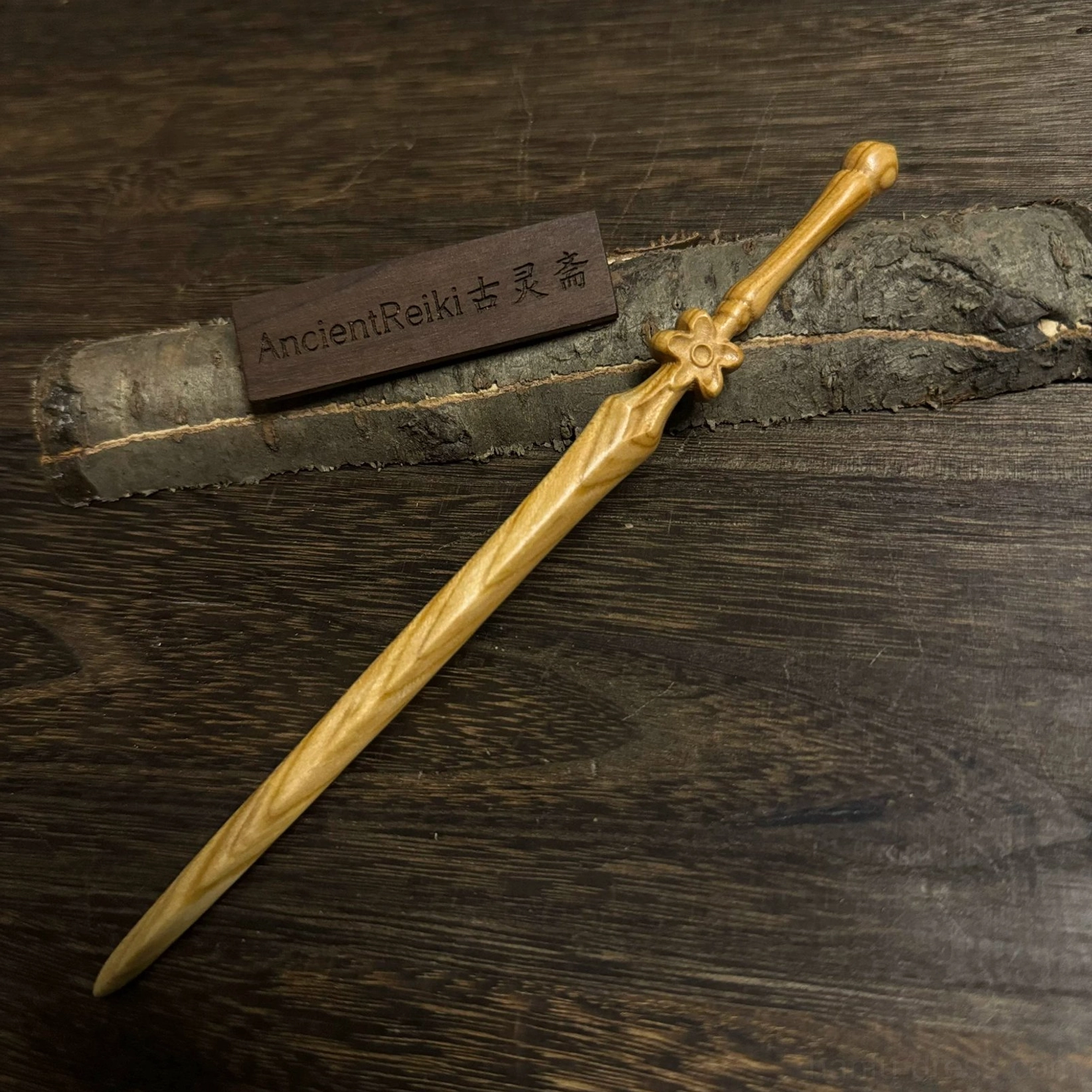 Cherry blossom sword-shaped wooden Chinese hair stick with carved blossom handle guard and striped blade texture displayed on a dark wooden surface