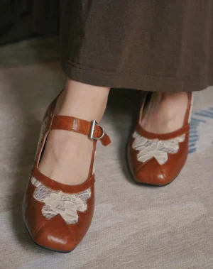 Front overhead view of chestnut vintage Mary Jane heels featuring square toe caps, matching floral lace decorations, smooth warm brown finish, and adjustable straps styled with a retro dark brown skirt