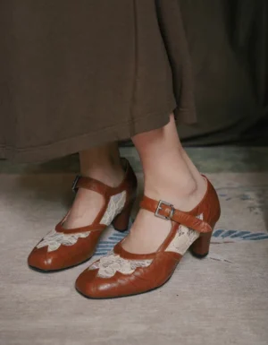 Chestnut vintage Qipao Mary Jane heels shown from a low side angle with floral lace appliqué, adjustable silver buckle ankle strap, warm brown upper, and chunky block heel styled with a dark brown skirt