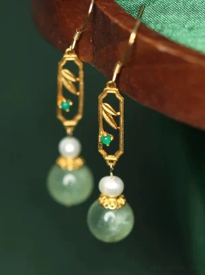 Angled view of Chinese bamboo pearl drop earrings featuring delicate gold-tone bamboo filigree, green accents, white pearl-style beads and smooth jade-tone drops