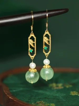 Traditional Chinese bamboo drop earrings with gold-tone openwork bamboo motif, green stone-style accents, pearl-style beads and jade-tone pendants displayed on an embroidered green tray