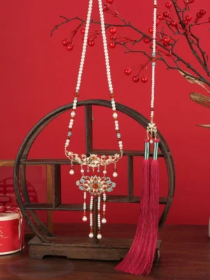 Chinese bridal yingluo necklace displayed on a wooden stand with gold cloisonne flowers pearl accents red agate beads and long wine red tassel