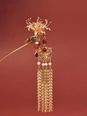 Front oblique close-up of a traditional Chinese butterfly tassel hair stick with gold floral ornament, blue butterfly, gemstone-style beads, faux pearls, and wheat-ear pendant on a dark red background