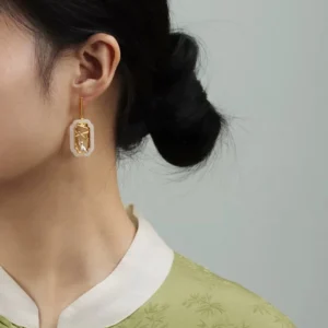Chinese cat pavilion stud earring worn with bamboo pattern cheongsam top, showing standing cat and gold lattice window design