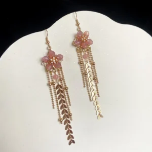 Chinese cherry blossom earrings with pink flower pendants, matte gold hardware, long mixed tassels, and hook closures on a scalloped display backdrop