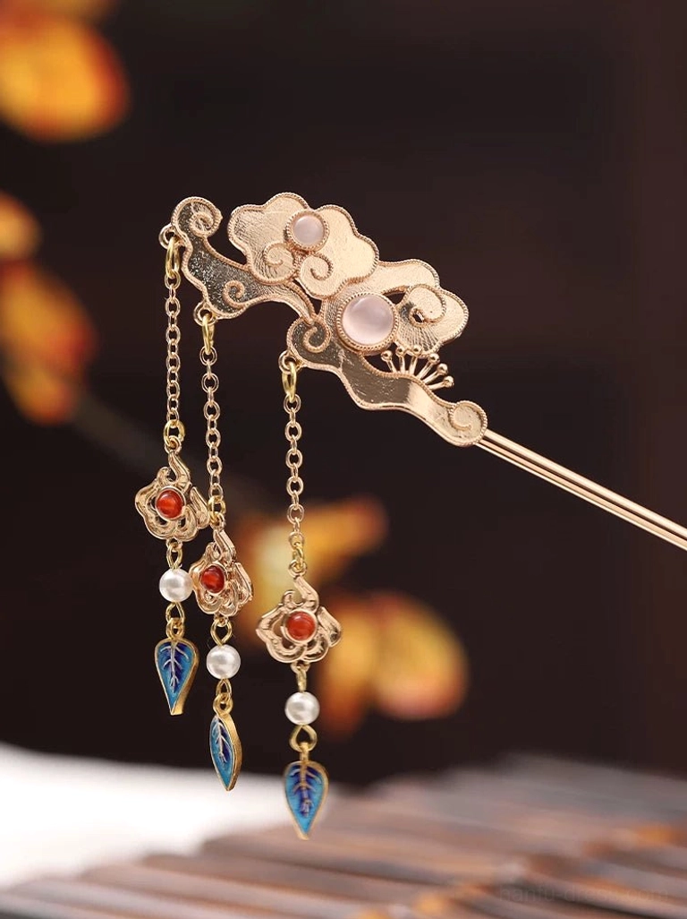 Close-up of a traditional Chinese cloud hair stick with gold-tone metal, pink gem-like inlays, red beads, white pearl details, and blue leaf-shaped tassel charms