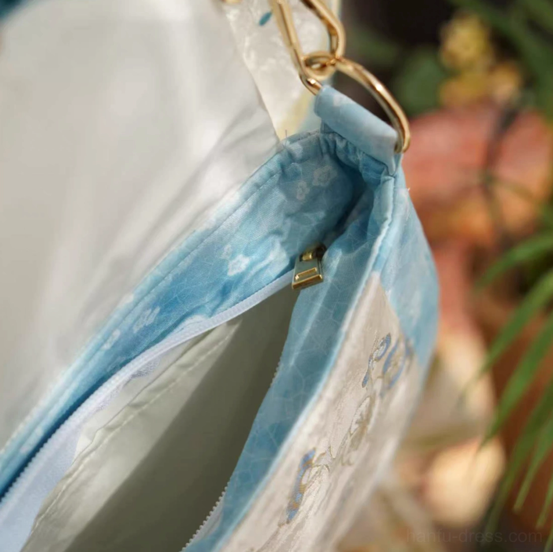 Open interior of a blue floral Chinese crossbody bag showing the light-colored lining, sky-blue inner trim, zippered main compartment, and gold-tone zipper hardware