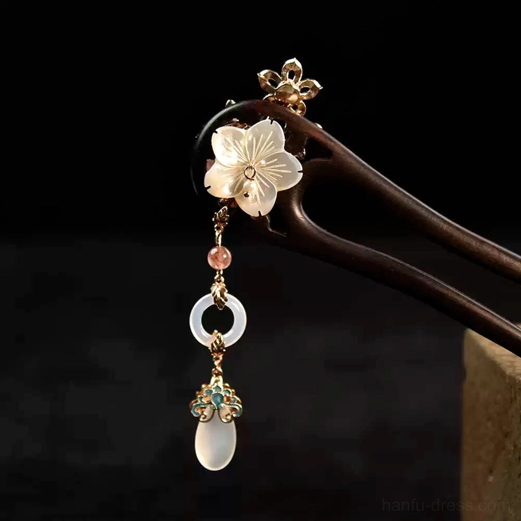 Chinese double-pronged hair stick with white flower ornament blush pink bead tassels and dark hairpin body on dark studio background