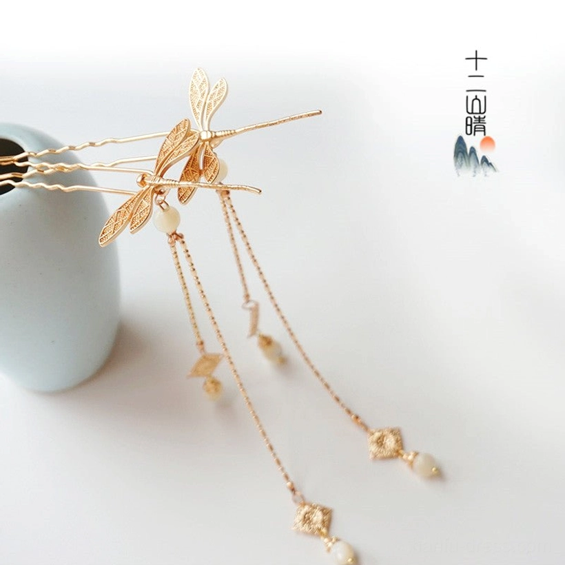 Chinese dragonfly tassel hair pins set in gold tone with white beads and long dangling chain pendants displayed beside a blue ceramic vase