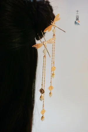 Gold dragonfly tassel hair pins worn on a traditional Chinese black hair bun with layered chains amber style pendants and white beads