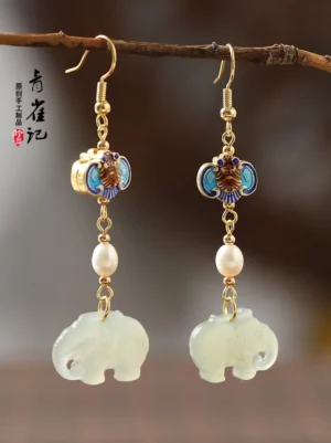 Chinese style elephant dangle earrings hanging from a wooden branch with milky white jade-tone elephant pendants, cloisonne bat charms, freshwater pearls, and gold ear wires