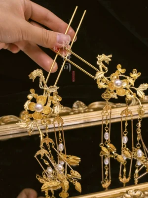 Gold-tone Chinese floral hair pins with white pearl accents and long dangling tassels displayed on a golden tray over black fabric