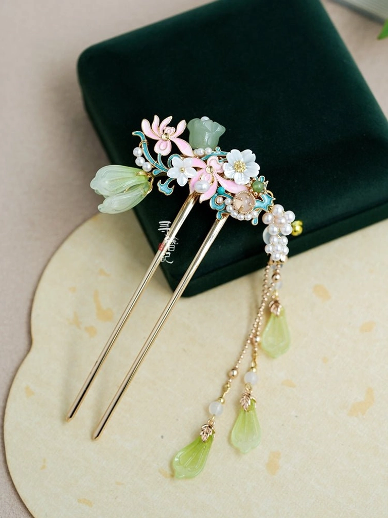 Traditional Chinese double pronged floral Hanfu hairpin with gold tone hair sticks, pink and white flower decorations, pearl clusters, green jade look pendants, blue enamel accents, and a long tassel displayed on a jewelry box