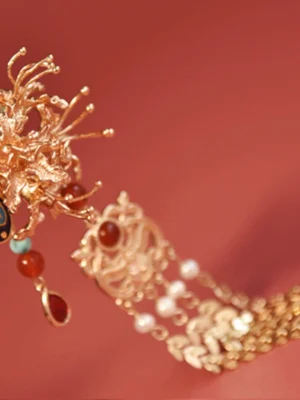 Side close-up of an ornate Chinese hair stick showing carved gold-toned flower detail, dangling beads, hollow metal chain ornament, and decorative tassel