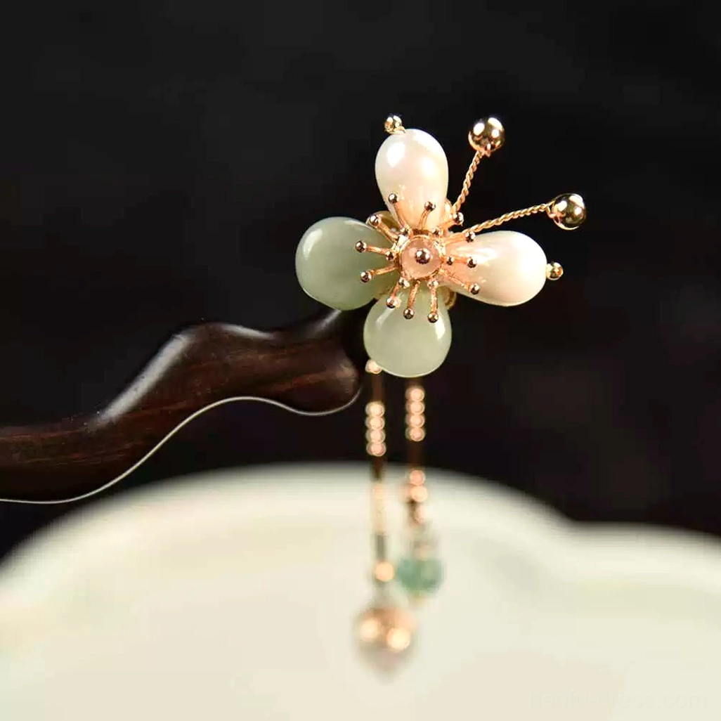 Close-up of a Chinese hair stick flower head showing pale jade-style plum blossom petals, golden stamens, and the beginning of its elegant dangling chain tassel