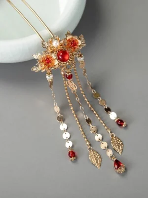 Ornate Chinese hair stick and tassel hairpin with gold-tone floral head, red gemstone-like accents, faux pearls, leaf charms, and dangling pendants displayed on a gray tabletop