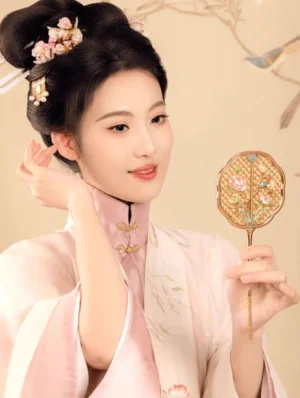 Chinese hand mirror held by a Hanfu woman wearing a light pink embroidered traditional dress, showing the ornate floral and blue bird decorated back
