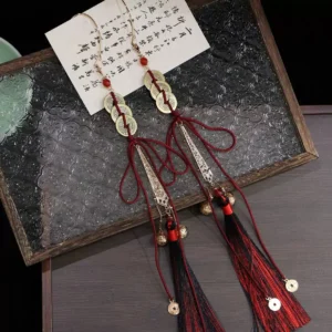Traditional Chinese Hanfu copper coin tassel ear cuff arranged on a vintage embossed glass tray with red and black tassels, carved metal charms, brass bells, and Chinese calligraphy paper