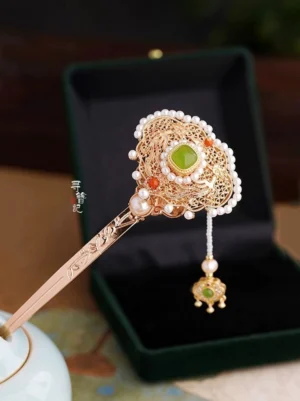 Three quarter view of an elegant Chinese Hanfu hairpin with carved gold toned hair stick filigree Ruyi ornament green jade centerpiece pearls and red bead details