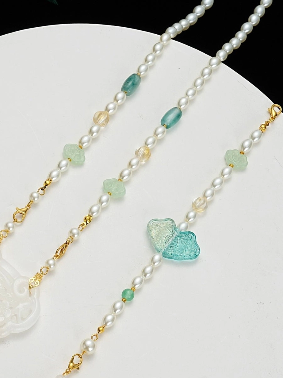 Close detail of a Chinese Hanfu necklace with pearl-like chains, gold spacer beads, light green jade beads, and a turquoise butterfly-shaped decorative ornament