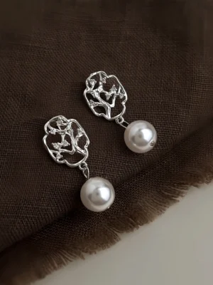 Chinese Hanfu pearl stud earrings with hollow plum branch window design on dark brown linen fabric