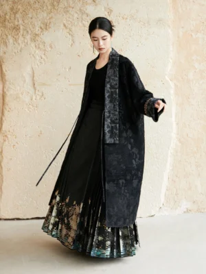 Three-quarter front view of a Chinese-inspired long jacquard coat showing the relaxed oversized fit, textured shawl lapel, and adjustable side tie closure