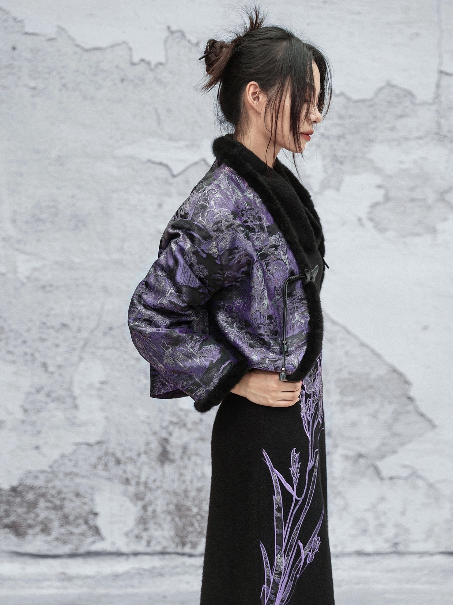 Three-quarter side view of a Chinese-inspired cropped jacket with traditional frog fasteners purple landscape jacquard fabric and black fuzzy trims