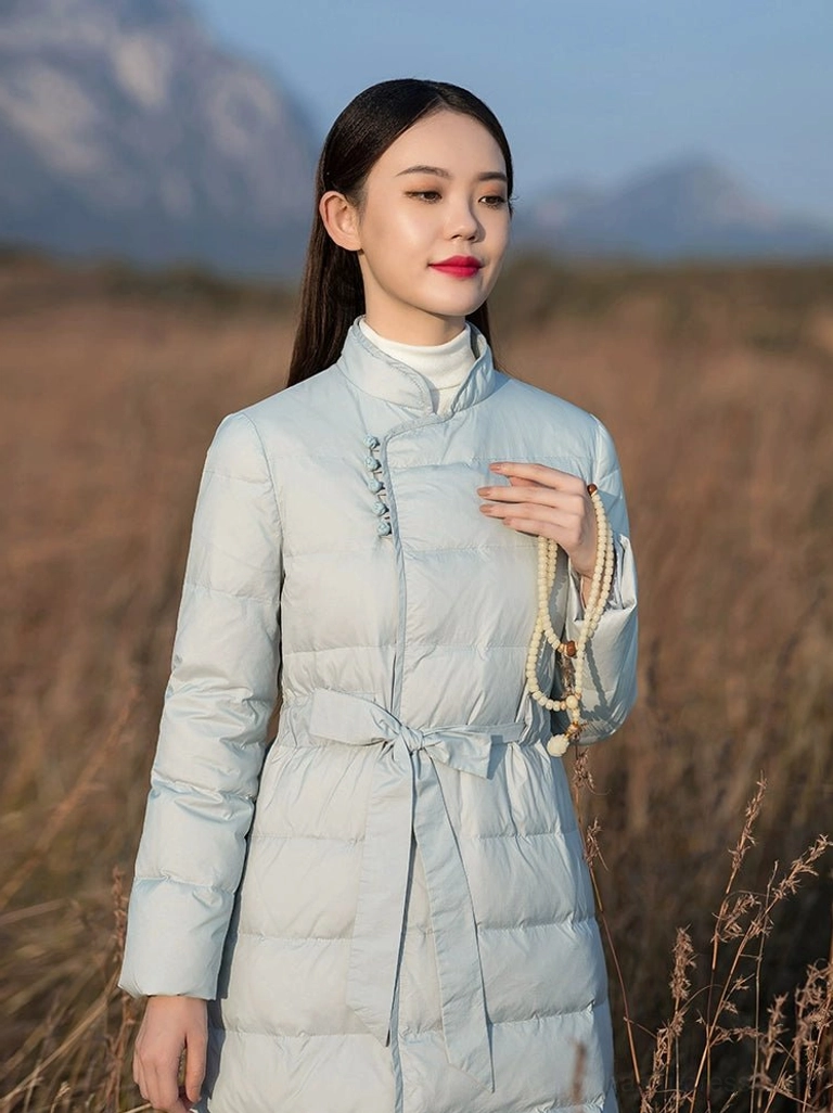 Close up front detail of a Chinese inspired women's down coat showing stand collar traditional frog buttons adjustable waist tie and quilted padded fabric