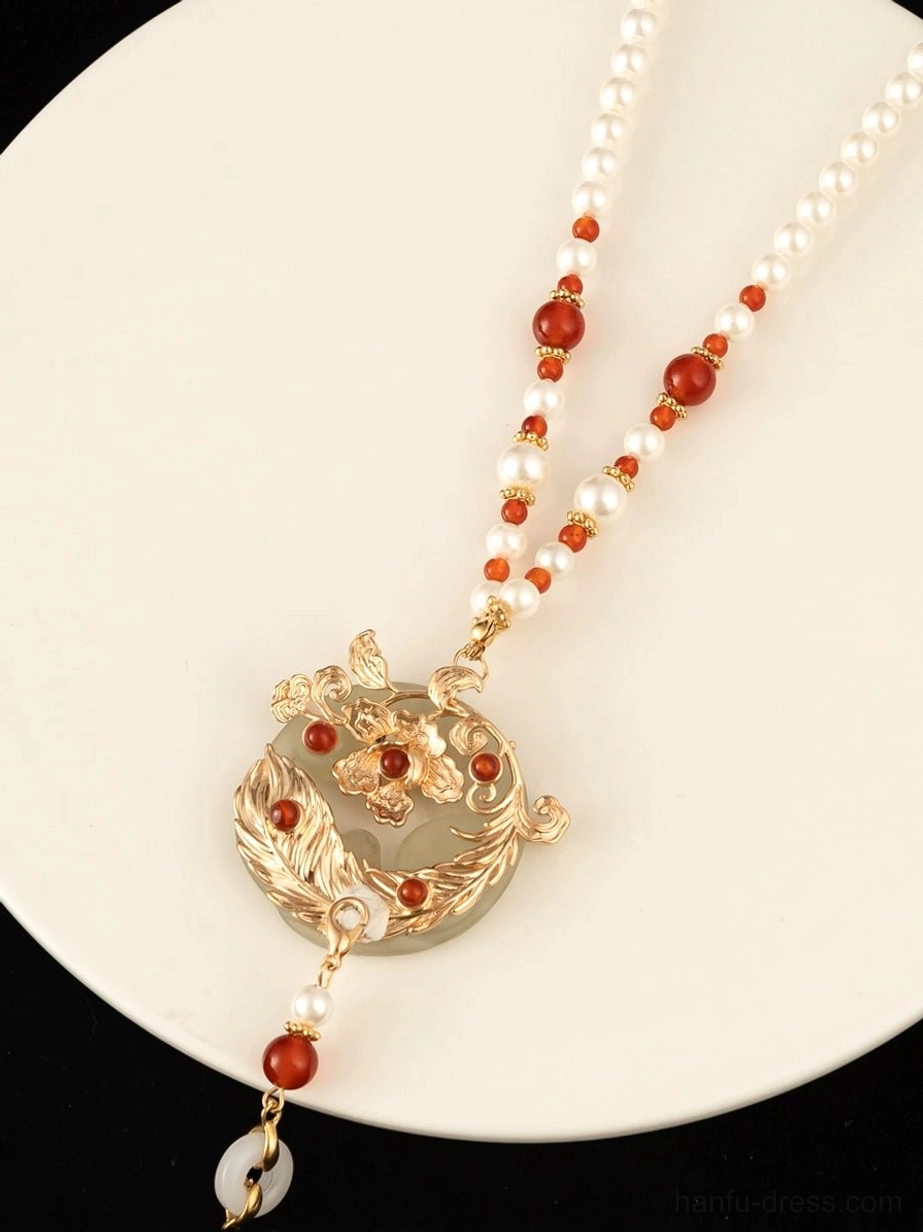 Close-up of Chinese necklace gold-tone floral carved pendant jade-tone disc and red agate bead details on ceramic tray