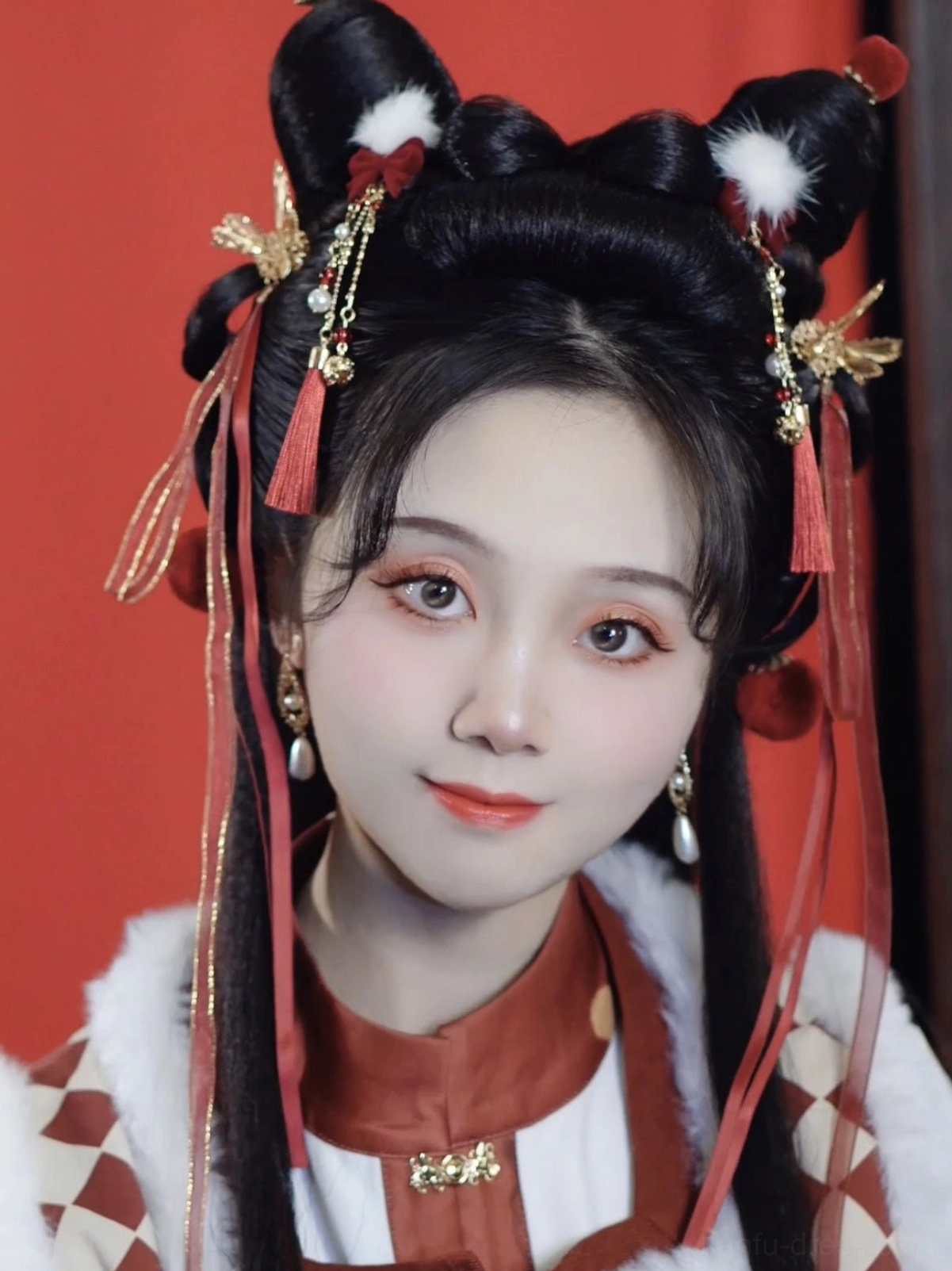 Model wearing a festive Chinese New Year Hanfu hair accessory set with red ribbons, tassels, white pom-poms and gold ornaments in double buns