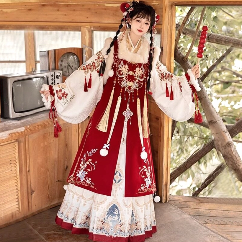 Side three-quarter view of a Chinese New Year Ming-style hanfu dress showing embroidered vest details, flowing printed skirt with red hem, festive hairstyle, and traditional seasonal styling
