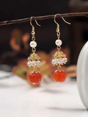 Chinese pumpkin dangle earrings shown in close-up with gold ear wires round white pearls filigree caps and clear sparkling crystal tassel details