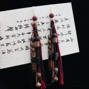 Chinese vintage red and black tassel drop earrings with wine red beads gold tone hooks decorative chains and handcrafted Hanfu jewelry details displayed on vintage calligraphy paper