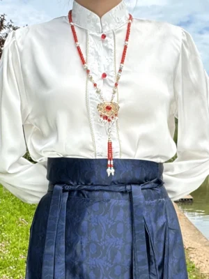 Hanfu model wearing a layered Chinese necklace with red gemstone accents Ruyi lock pendant and red tassel over a white stand collar top