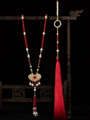 Chinese Ruyi lock necklace with red agate beads freshwater pearls gold tone pendant and long red tassel displayed on a traditional wooden jewelry stand