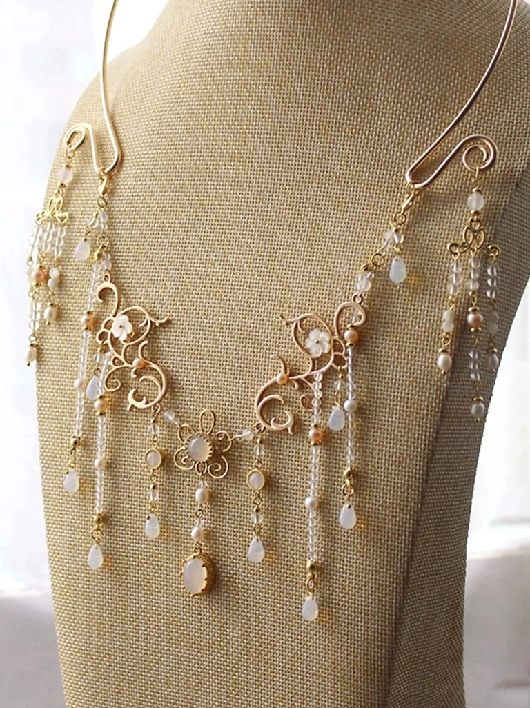 Chinese-style gold collar necklace displayed on a beige mannequin with symmetrical floral filigree, delicate beaded tassels, and a refined central pendant