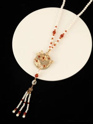 Chinese style long necklace with red and white beaded chain jade-tone pendant and multi-strand tassel on white ceramic tray
