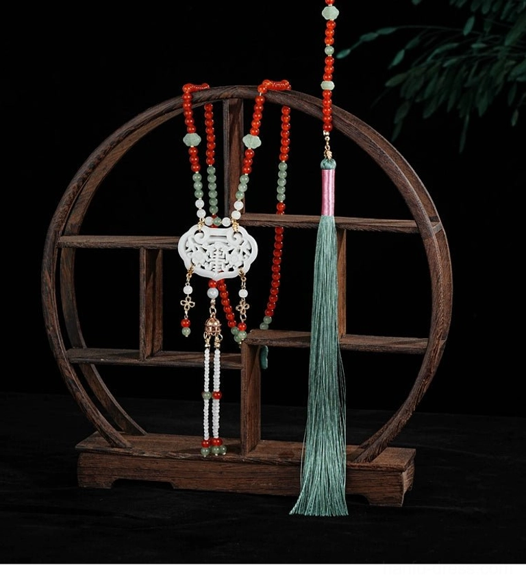 Chinese style tassel necklace displayed on a wooden shelf with red beaded chain, jade pendant, decorative beads, and long cyan tassel