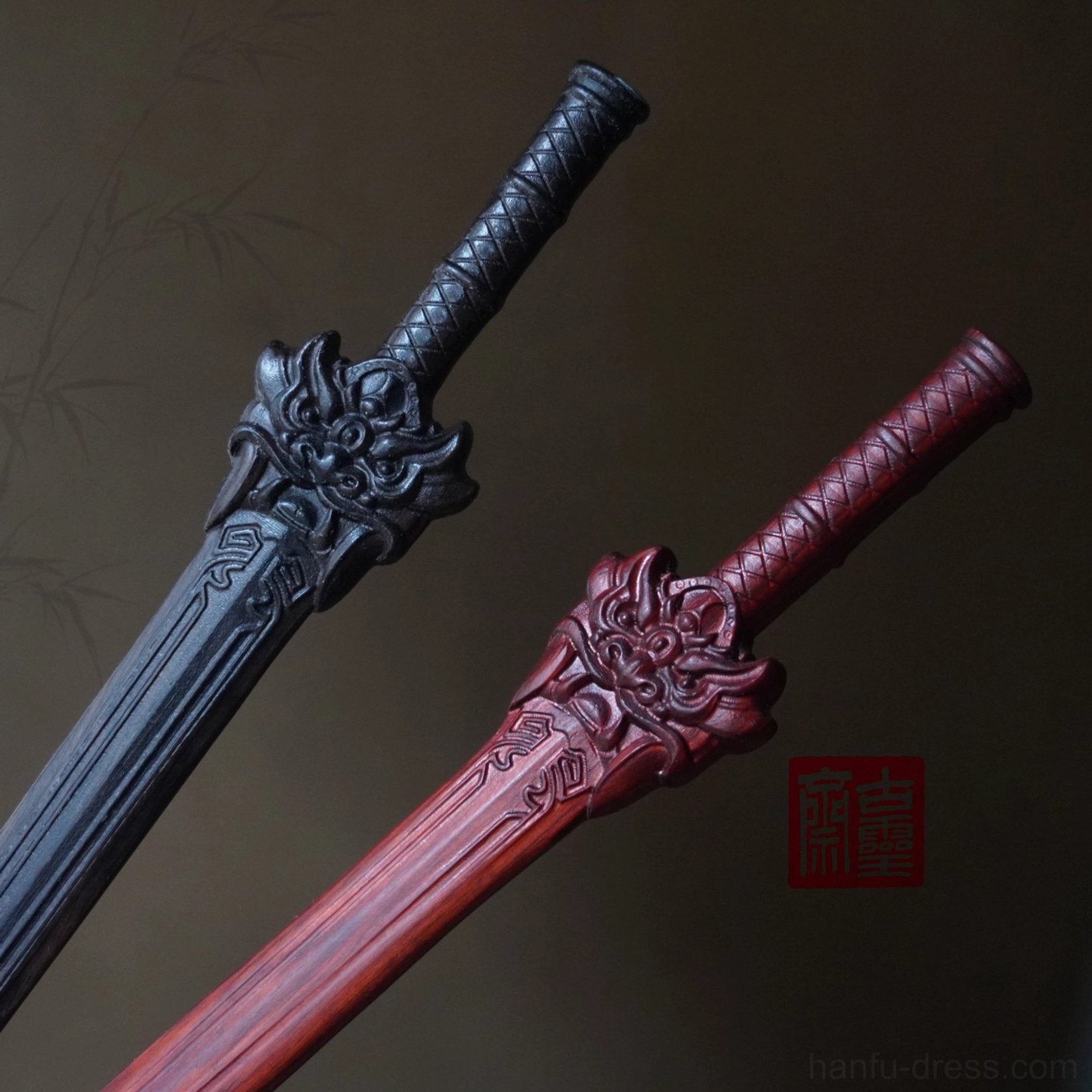 Chinese sword hair stick pair displayed at an angle showing black and wine red finishes, sculpted mythical beast heads, and carved blade details