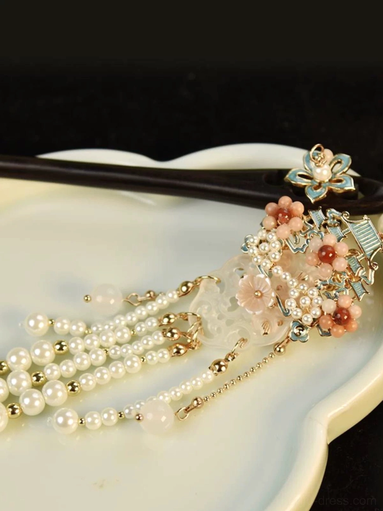 Chinese tassel hair stick displayed on a white ceramic tray with pink enamel flower ornament, carved jade-inspired pendant, pearl strands, and gold-tone chain tassels