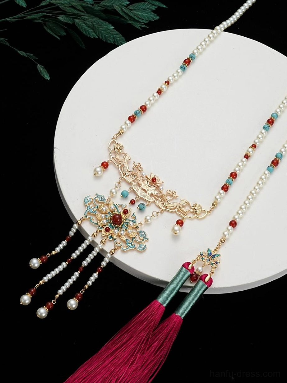 Side flat lay view of a Chinese tassel hanfu necklace with pearl-style chain, red and turquoise beads, gold cloisonne pendant, and rose-red tassel on a white display plate
