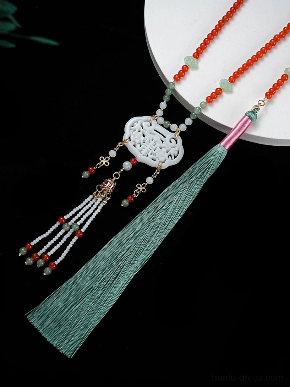 Close-up of Chinese tassel necklace showing carved jade lock pendant, red and green beaded chain, decorative beads, and long cyan tassel